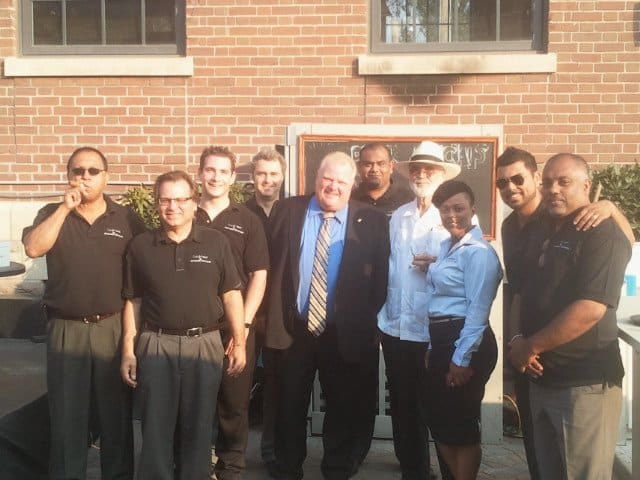 group of people standing in front of black chalkboard with brown border, brown brick wall with two windows